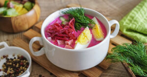 Cold beetroot soup with sausage and vegetables on a rustic wooden table.