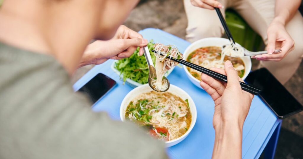 Shutterstock Close up of couple eating pho soup on a sidewalk in Vietnam