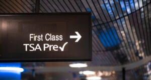 Overhead sign showing security check point lanes designated for first class and TSA Precheck passengers. Illuminated white text on black banner. Silver metallic ceiling in bokeh in background.