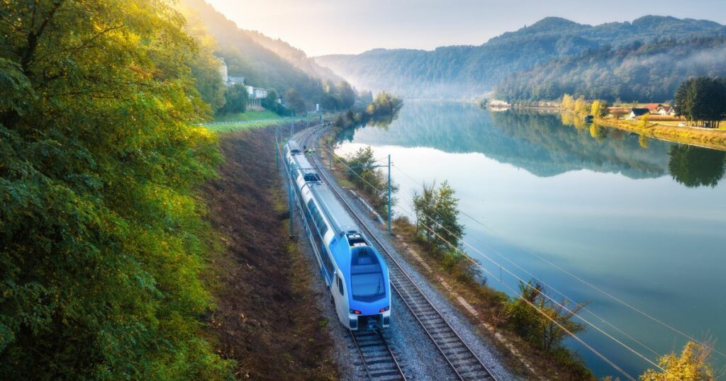 Shutterstock Aerial view of blue modern high speed train moving near river in alpine mountains in fog at sunrise in autumn in Slovenia