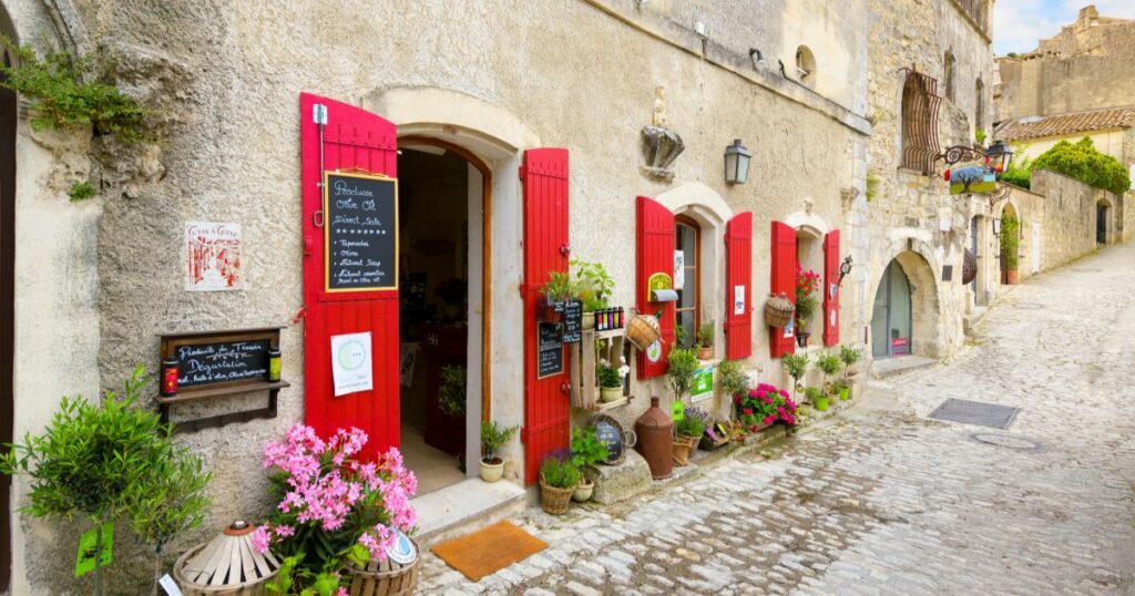 Shutterstock Les Baux-de-Provence, France - September 21 2023: A charming boutique market with bright red shutters in the medieval old town of Les Baux, in the Bouches-du-Rhône Provence-Alpes-Côte d'Azur region