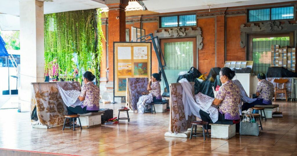 Shutterstock Artisans are seated in a beautifully decorated studio crafting detailed patterns, showcasing traditional Indonesian techniques in a vibrant and cultural setting