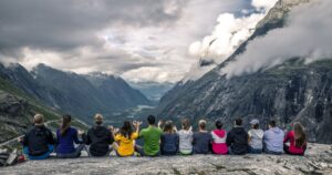 Group of young people sitting on the plateau on top of mountain and looking forward on the beautiful valley full of clouds, Trollstigen, Norway