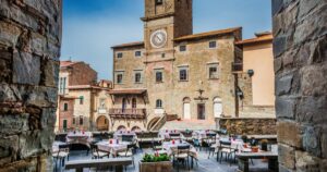 Cortona Communal Palace with renaissance tower clock seen from a narrow street in the historic center, an old medieval town in Tuscany, Italy