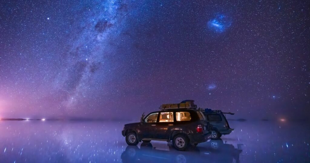 Shutterstock Milky way and starry sky over the salt flat of Uyuni, Bolivia, with 2 SUVs parked on the reflective lake surface.