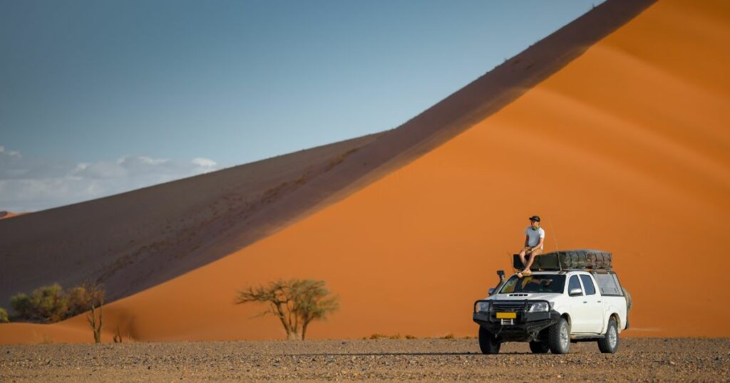 Shutterstock Young Asian man tourist sitting on camper car near orange sand dune landscape. Travel desert in Namibia, Africa.