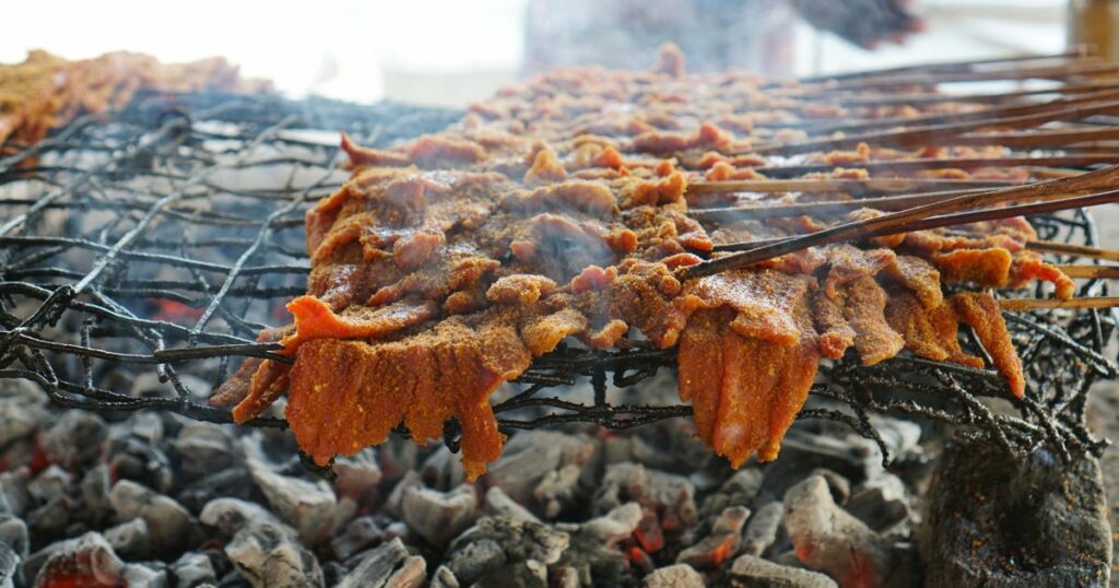 Sticks of spicy beef Suya sticks on an open grill