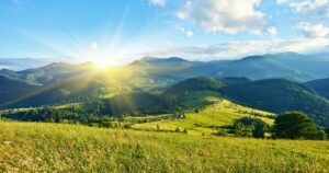Idyllic landscape in the Alps with fresh green meadows and blooming flowers and snow-capped mountain tops in the background