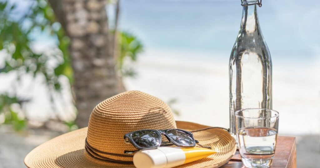 Shutterstock Glass bottle of water, straw hat, sun glasses and sunscreen on the beach in the Maldives