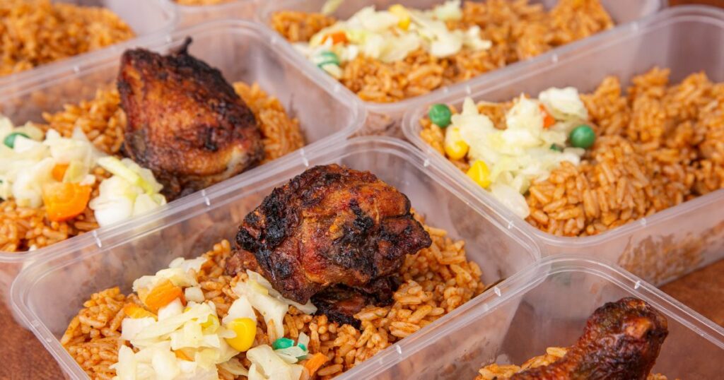 Plates of Jollof rice with chicken and sprinkled salad in transparent plate on the street of Lagos