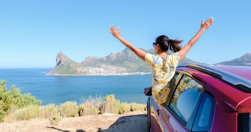 Shutterstock Woman in a yellow floral dress joyfully leans out of a red car with arms raised