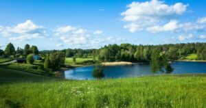 Swedish countryside landscape with lush green field and lake on warm summer day, Lake Foxen in Värmland, Sweden