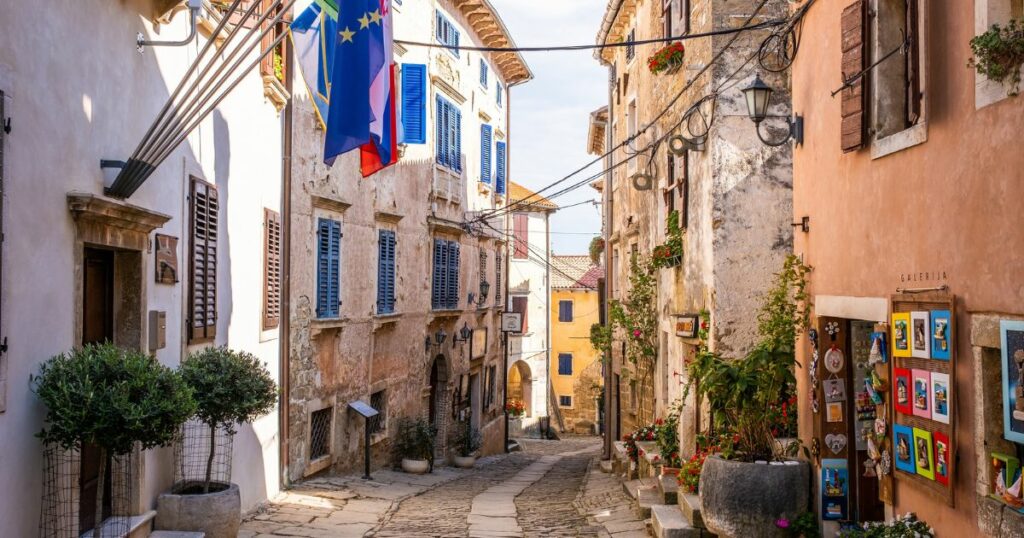 Shutterstock Grožnjan, Croatia, September 30th, 2023: A charming, narrow street in historic Grožnjan, featuring colorful shutters, potted plants, and European flags.