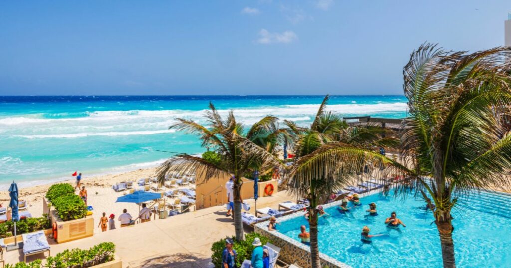 Shutterstock Palm trees swaying near resort pool overlooking turquoise waves of Caribbean sea in Cancun, Mexico