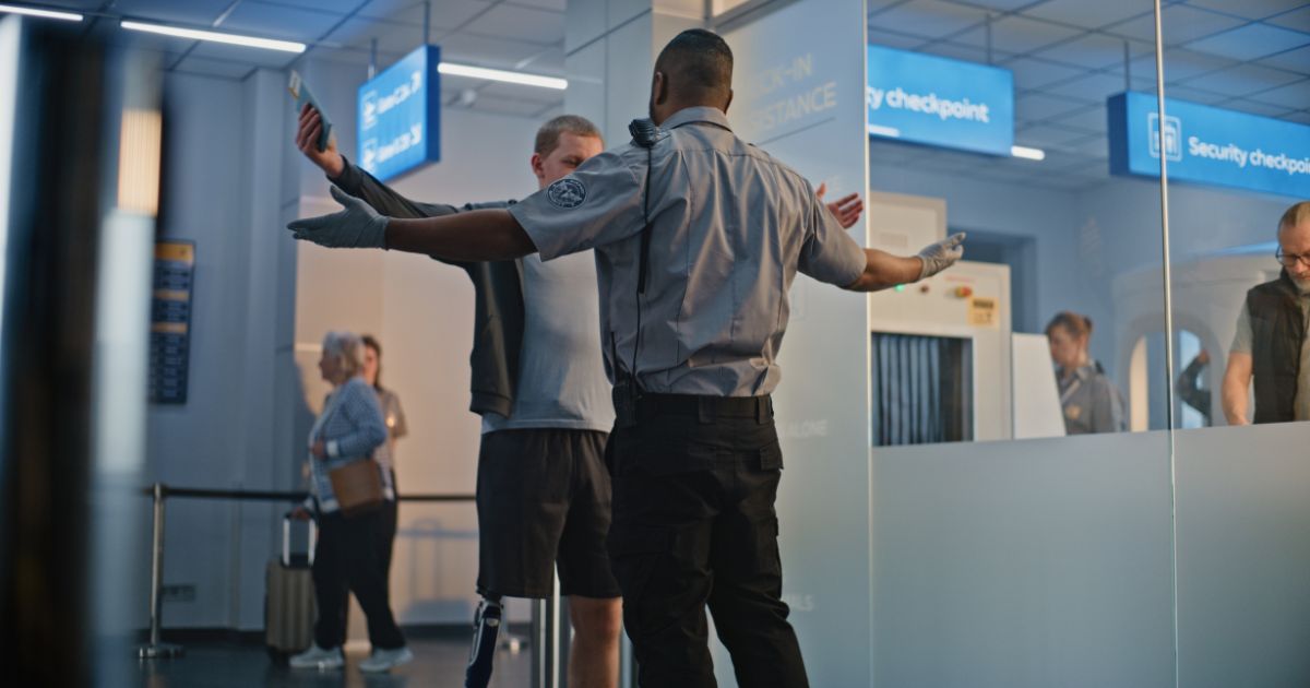 Security Checkpoint: African American TSA Officer Checking Young Man with Prosthetic Leg in Airport Terminal. Passenger Screening Procedures for Boarding Flight. Traveler with Disability Going on Trip
