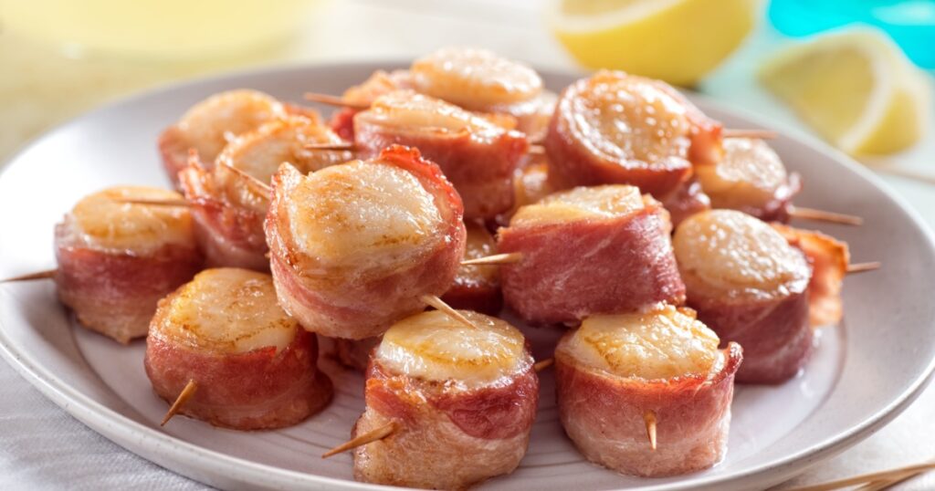 A plate of delicious bacon wrapped scallops with lemon.