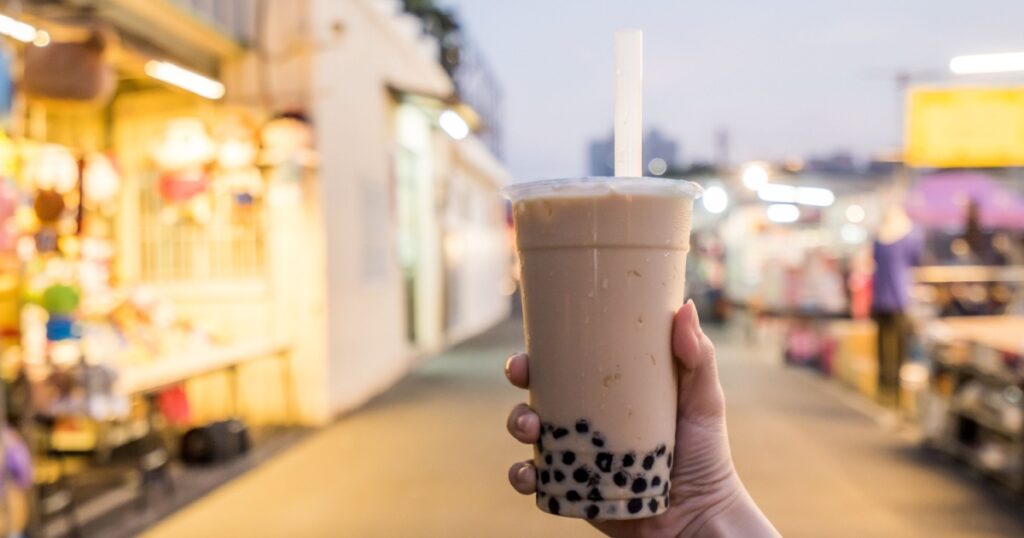 A young woman is holding a plastic cup of bubble milk tea with a straw at a night market in Taiwan