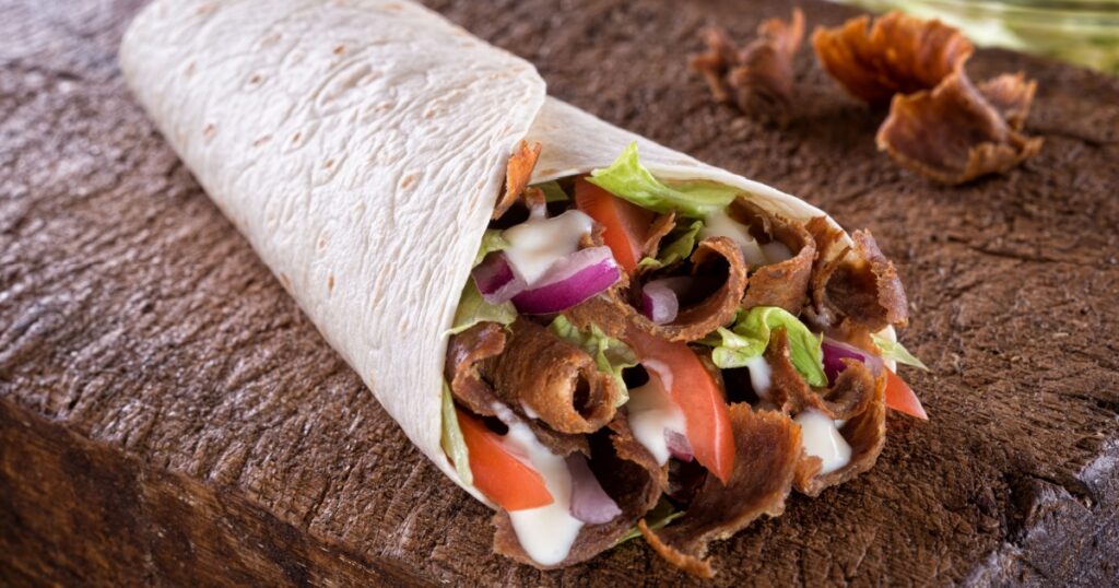 A delicious doner donair kebab wrap with spicy meat, lettuce, tomato, red onion and sauce.