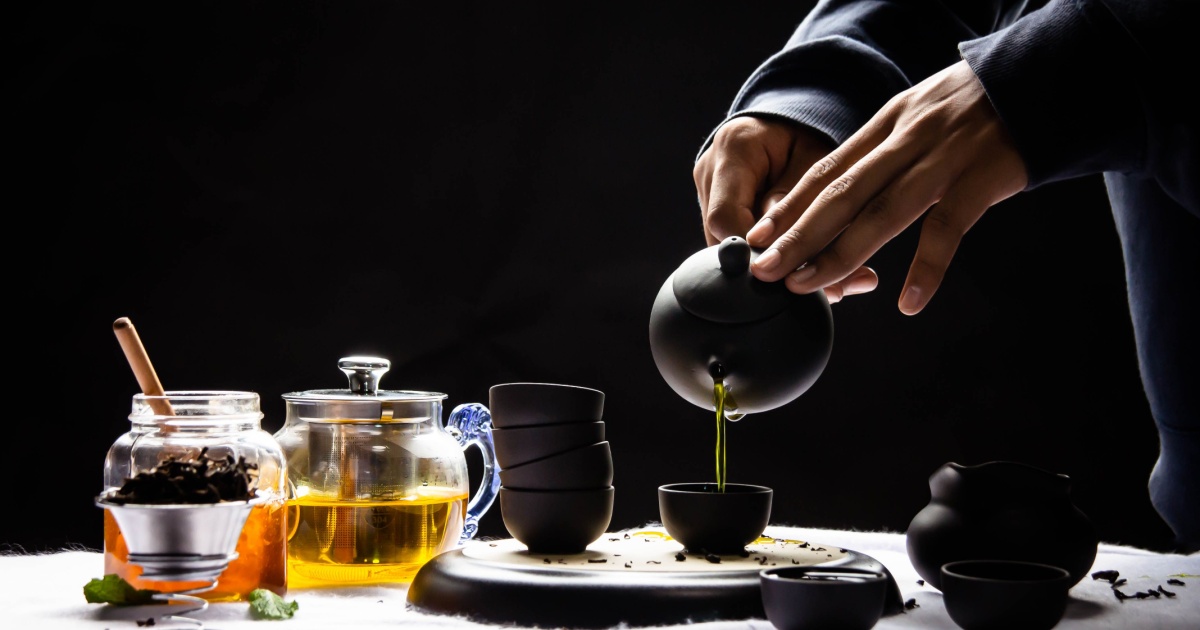 glass and cup on a black background and hands pouring tea