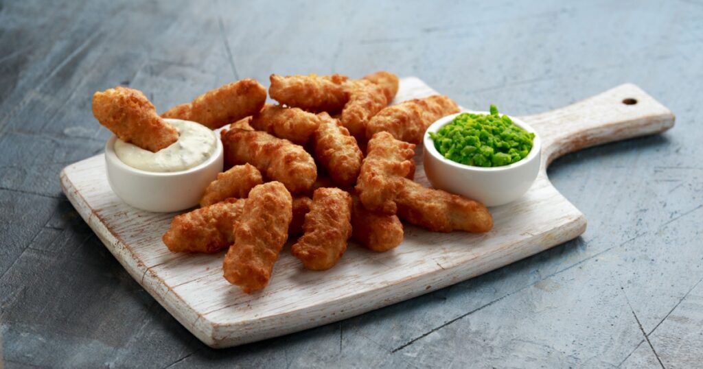 Battered Haddock fish, mini fingers with mashed peas, tartar sauce on white wooden board