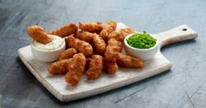 Battered Haddock fish, mini fingers with mashed peas, tartar sauce on white wooden board