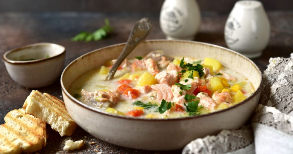 Chowder - thick potato soup with trout ( salmon ) and cream in a white bowl on a dark slate, stone or concrete background.