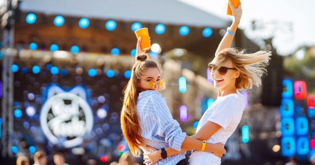 Two female friends with drinks in hands and having fun at the music festival