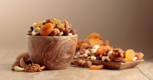 Dried fruits and nuts on a beige ceramic table. The mix of nuts, apricots, and raisins in a wooden bowl.