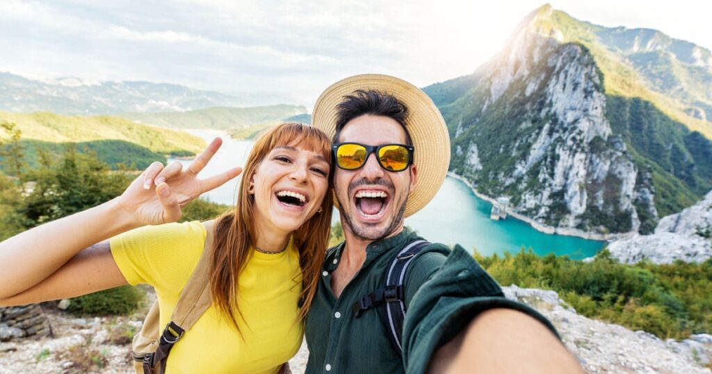 Happy couple taking selfie pic with smart mobile phone on top of the mountain