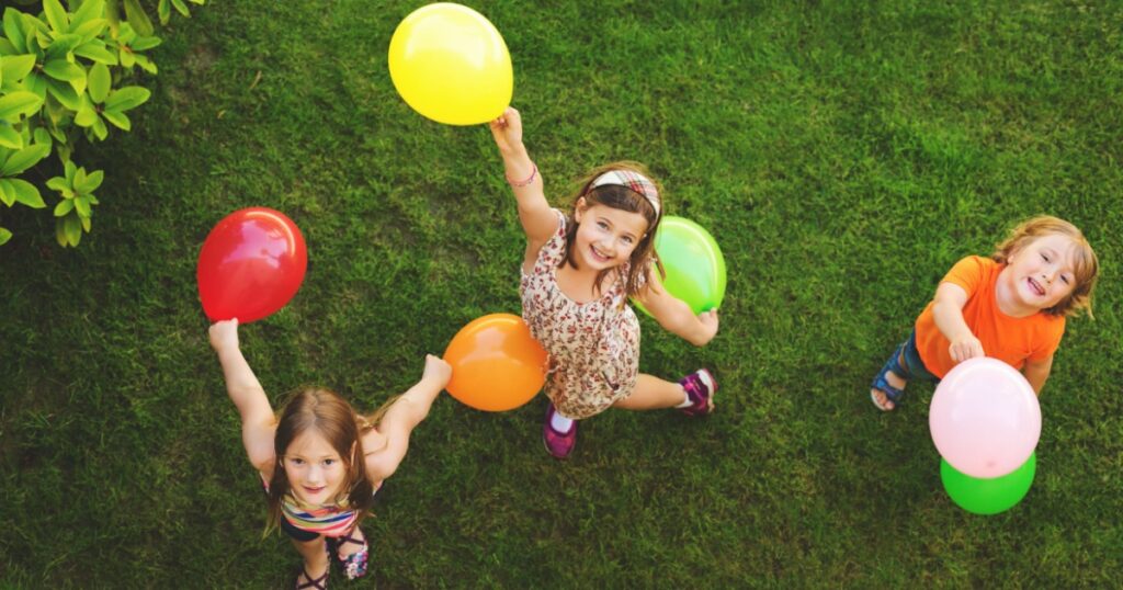 Three happy little kids playing with colorful balloons outdoors, top view