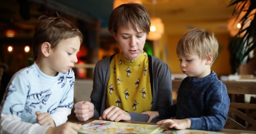 Mother with her sons choosing dishes at table in the restaurant