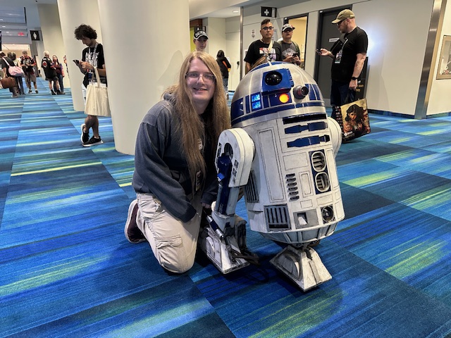 A smiling Connor Blum of Harrison Excelsior, 501st Legion crouches beside Artoo Blum, a custom-built R2-D2 replica he built complete with lights and sound at Fan Expo Canada.
