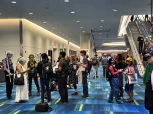 A group of Fan Expo attendees dressed in a variety of costumes, chatting and taking photos in a bright convention hallway.
