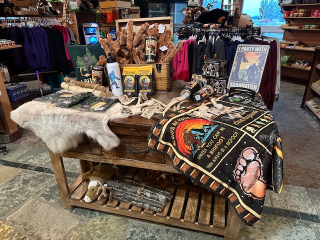 Gift shop display at Pike’s Waterfront Lodge featuring Alaskan souvenirs, including Bigfoot merchandise, blankets, furs, and locally themed products on a rustic wooden table.