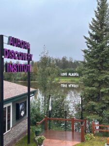 View of Pike’s Aurora Discovery Institute with purple signage, overlooking the Chena River pond and the iconic “LOVE ALASKA” sign in the distance.