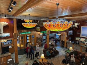 Lobby of Pike’s Waterfront Lodge with rustic log walls, stained-glass chandeliers, mounted taxidermy, and groups of guests gathered in a warm, welcoming atmosphere.