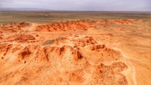 Expansive view of the Flaming Cliffs in Mongolia’s Gobi Desert, showcasing dramatic orange-red rock formations against a vast, arid plain.