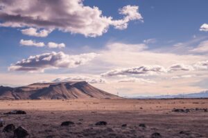 A vast dry plain dotted with dark rocks, leading to a flat-topped mountain under a wide sky filled with layered clouds.