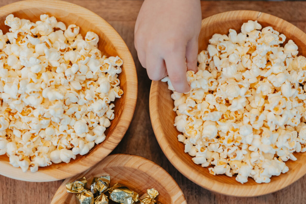 Close-up of popcorn in two wooden bowls with a child’s hand reaching in, showcasing the craftsmanship of Alaskan birch bowls.