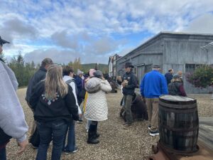 Group of visitors gathered around a guide outside rustic buildings at Gold Dredge 8, learning about Alaska’s gold mining history.
