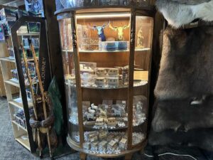 A glass display case filled with handcrafted Alaskan souvenirs, including figurines, ornaments, and miniature cabins.