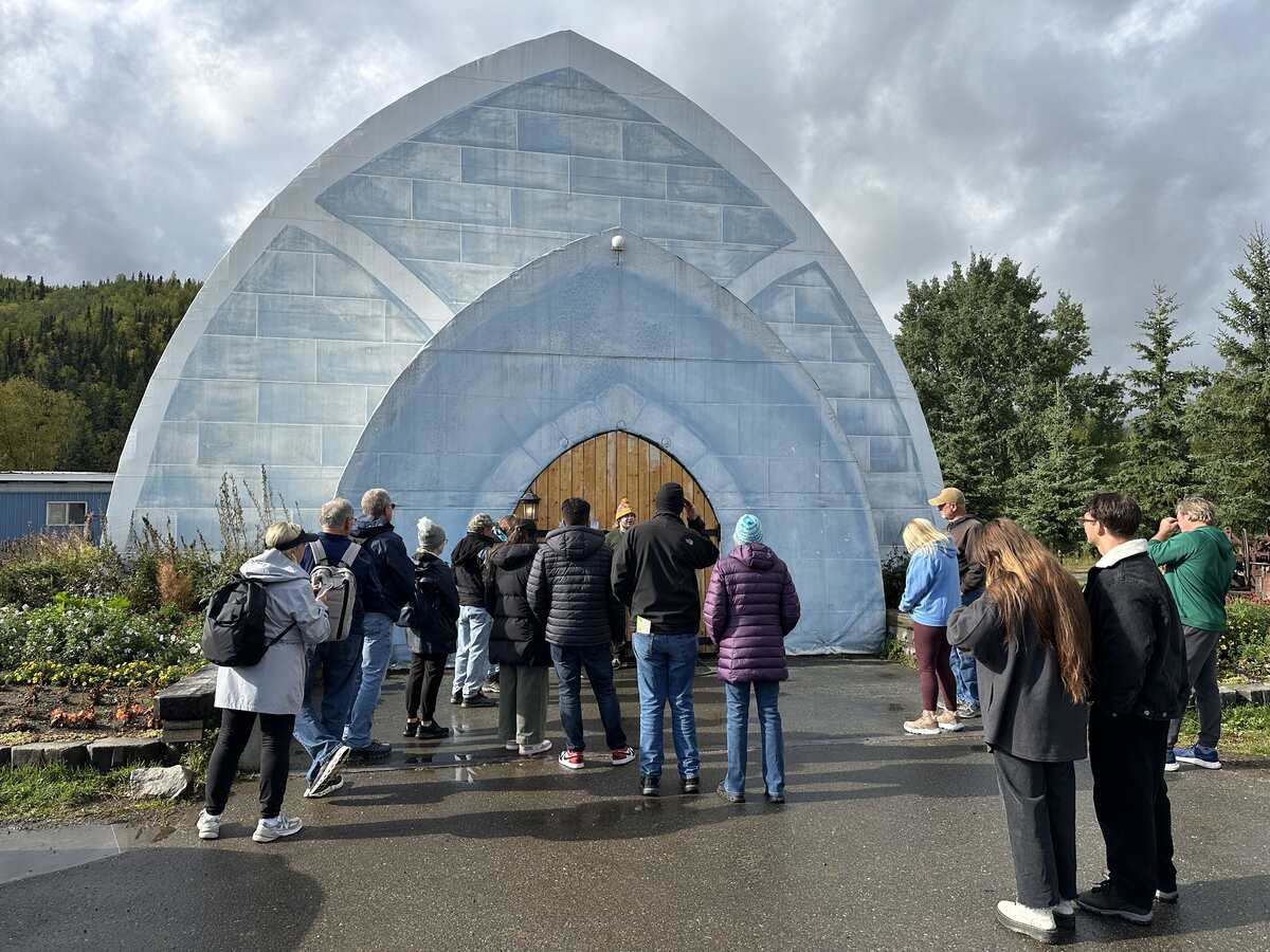 A group of visitors stands outside the arched blue entrance of the Aurora Ice Museum at Chena Hot Springs.