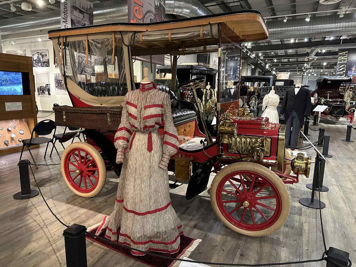 Antique auto paired with an ornate gown from the early 1900s, reflecting an elegant past.