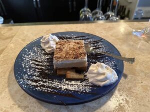 A slice of Ekmek. A layered Greek dessert with whipped cream, chopped nuts, and chocolate drizzle on a blue plate at Bobby’s Restaurant in Fairbanks.