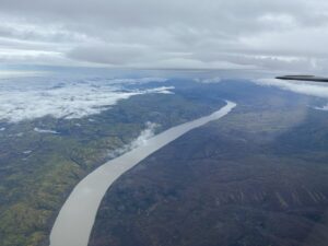 The wide, winding Yukon River seen from above, carving its way through forested hills.