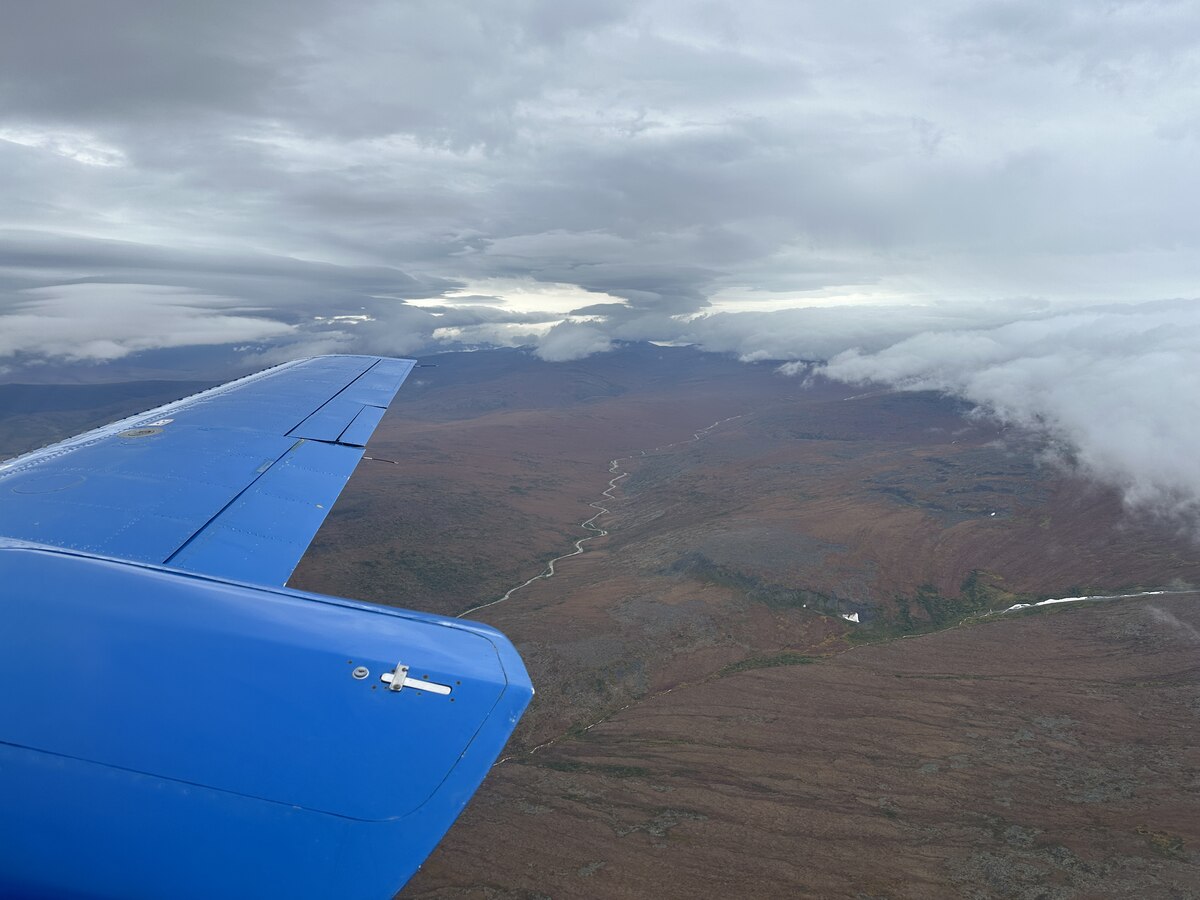 Aerial view of Alaska’s rugged tundra landscape with winding rivers, seen from a small plane window.