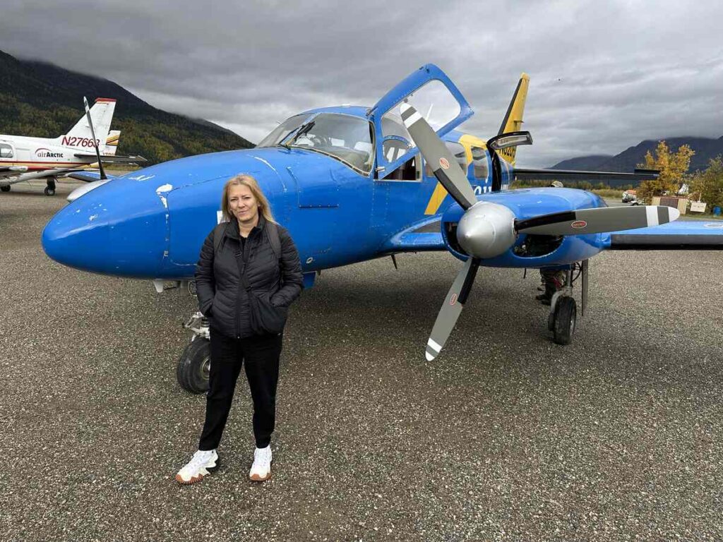Traveller standing in front of a small blue twin-propeller plane used for Arctic Circle flight tours.