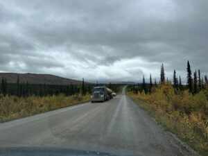 Large oil truck driving down the gravel Dalton Highway lined with autumn trees and endless wilderness. Convoys of oil trucks speed along the Dalton, sharing the narrow, rugged road with adventurous travellers.