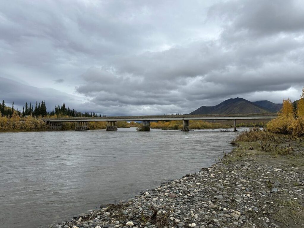 The long Yukon River Bridge stretching across wide waters with mountains and autumn trees in the background.