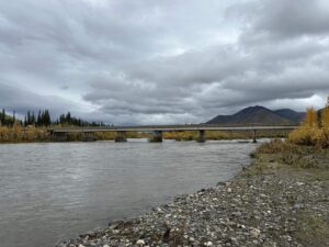 The long Yukon River Bridge stretching across wide waters with mountains and autumn trees in the background.
